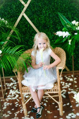  Beyaz elbiseli, sarı saçlı, beyaz çiçekli, nilüferli ve orkideli yeşil tropikal bitkileri olan tatlı bir kız.