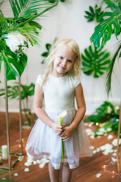 白いドレスと白い花 ユリと緑の熱帯植物を背景に蘭の花で金髪のかわいい女の子 — ストック写真