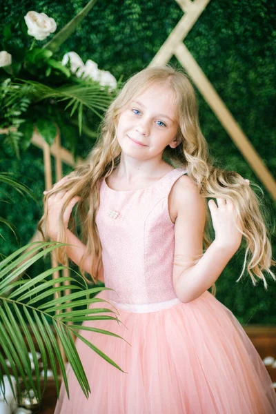 ピンクのドレスと白い花の長いブロンドの髪のかわいい女の子 緑の熱帯植物を背景にユリと蘭 — ストック写真