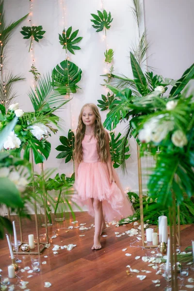 ピンクのドレスと白い花の長いブロンドの髪のかわいい女の子 緑の熱帯植物を背景にユリと蘭 — ストック写真