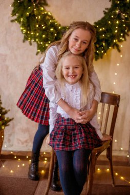 Sarışın, kıvırcık saçlı, klasik okul kıyafetleriyle gişelere yasaklı güzel kız kardeşler duvarda klasik bir iç mekan olan çam iğnelerinden oluşan büyük bir Noel çelenginin yanında. Noel havası 