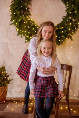 Sarışın, kıvırcık saçlı, klasik okul kıyafetleriyle gişelere yasaklı güzel kız kardeşler duvarda klasik bir iç mekan olan çam iğnelerinden oluşan büyük bir Noel çelenginin yanında. Noel havası 