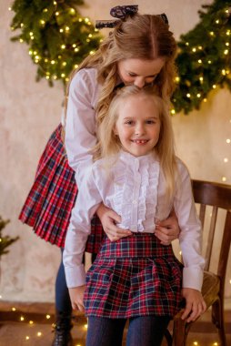 Sarışın, kıvırcık saçlı, klasik okul kıyafetleriyle gişelere yasaklı güzel kız kardeşler duvarda klasik bir iç mekan olan çam iğnelerinden oluşan büyük bir Noel çelenginin yanında. Noel havası 