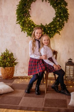 Sarışın, kıvırcık saçlı, klasik okul kıyafetleriyle gişelere yasaklı güzel kız kardeşler duvarda klasik bir iç mekan olan çam iğnelerinden oluşan büyük bir Noel çelenginin yanında. Noel havası 