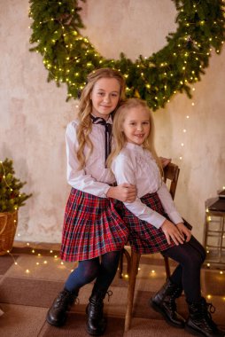 Sarışın, kıvırcık saçlı, klasik okul kıyafetleriyle gişelere yasaklı güzel kız kardeşler duvarda klasik bir iç mekan olan çam iğnelerinden oluşan büyük bir Noel çelenginin yanında. Noel havası 