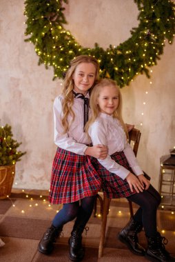 Sarışın, kıvırcık saçlı, klasik okul kıyafetleriyle gişelere yasaklı güzel kız kardeşler duvarda klasik bir iç mekan olan çam iğnelerinden oluşan büyük bir Noel çelenginin yanında. Noel havası 