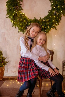 Sarışın, kıvırcık saçlı, klasik okul kıyafetleriyle gişelere yasaklı güzel kız kardeşler duvarda klasik bir iç mekan olan çam iğnelerinden oluşan büyük bir Noel çelenginin yanında. Noel havası 