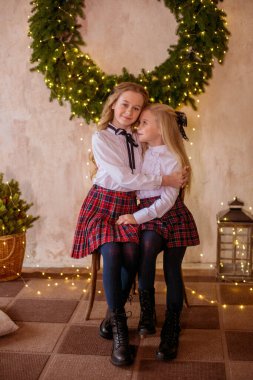 Sarışın, kıvırcık saçlı, klasik okul kıyafetleriyle gişelere yasaklı güzel kız kardeşler duvarda klasik bir iç mekan olan çam iğnelerinden oluşan büyük bir Noel çelenginin yanında. Noel havası 