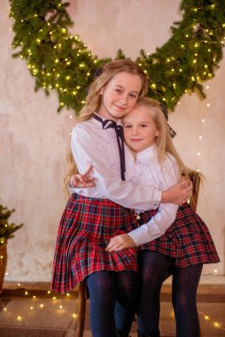 Sarışın, kıvırcık saçlı, klasik okul kıyafetleriyle gişelere yasaklı güzel kız kardeşler duvarda klasik bir iç mekan olan çam iğnelerinden oluşan büyük bir Noel çelenginin yanında. Noel havası 