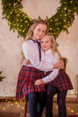 Sarışın, kıvırcık saçlı, klasik okul kıyafetleriyle gişelere yasaklı güzel kız kardeşler duvarda klasik bir iç mekan olan çam iğnelerinden oluşan büyük bir Noel çelenginin yanında. Noel havası 