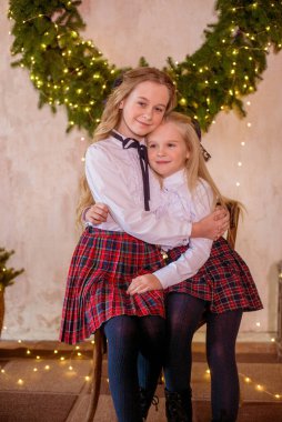 Sarışın, kıvırcık saçlı, klasik okul kıyafetleriyle gişelere yasaklı güzel kız kardeşler duvarda klasik bir iç mekan olan çam iğnelerinden oluşan büyük bir Noel çelenginin yanında. Noel havası 