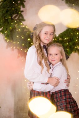 Sarışın, kıvırcık saçlı, klasik okul kıyafetleriyle gişelere yasaklı güzel kız kardeşler duvarda klasik bir iç mekan olan çam iğnelerinden oluşan büyük bir Noel çelenginin yanında. Noel havası 