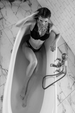 Siyah bikinili, siyah saçlı çekici bir genç kız ve banyoda zincirli ve parlak taşlardan yapılmış büyük bir moda mücevheri. Boş & Spa 