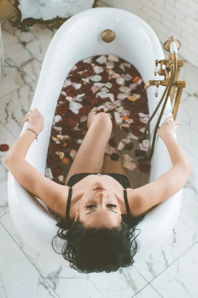 迷人的小女孩 黑头发 黑色比基尼 浴缸里满是玫瑰花瓣 休闲和温泉 — 图库照片