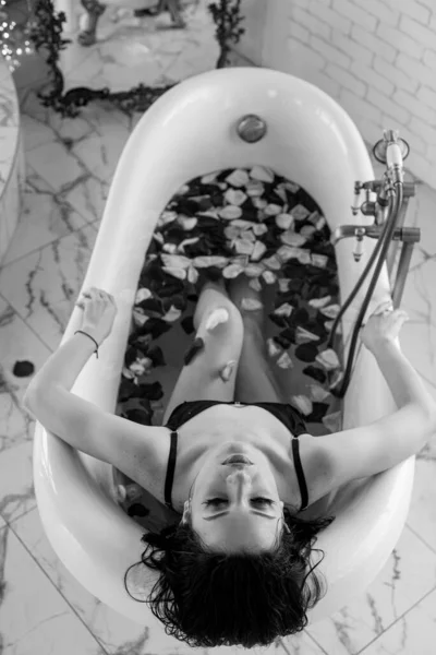 迷人的小女孩 黑头发 黑色比基尼 浴缸里满是玫瑰花瓣 休闲和温泉 — 图库照片
