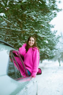 Pembe kazaklı genç kız kışın kar altında araba camından dışarı bakıp gülüyor. 