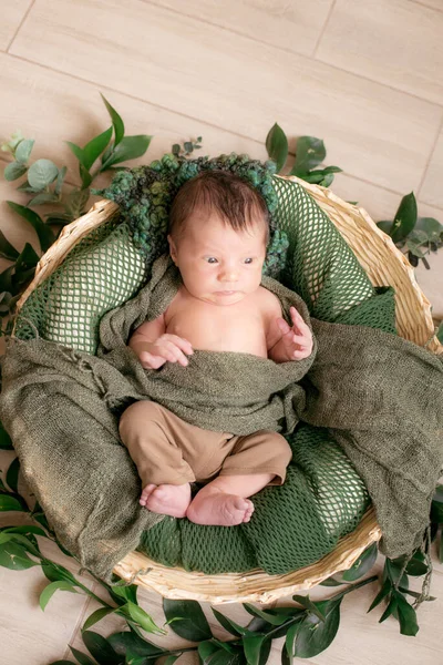 可爱的小宝宝在一个柳条篮装饰绿色树枝在绿色针织毛毯在家里的轻木制背景 — 图库照片