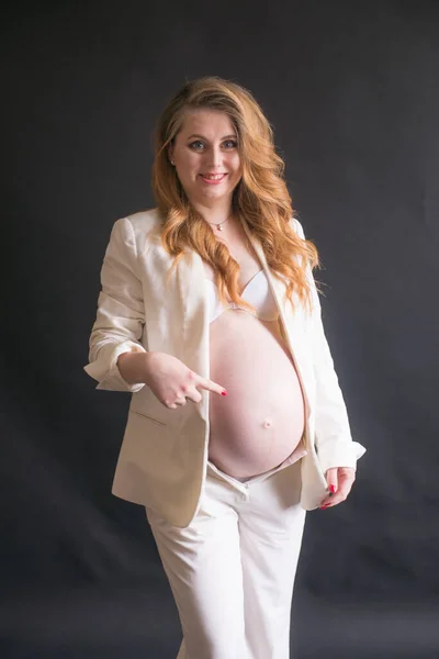 黒の背景に白いズボンのスーツに長い赤い髪の若いかわいい妊娠中の女性 幸せな母親 母の日 — ストック写真