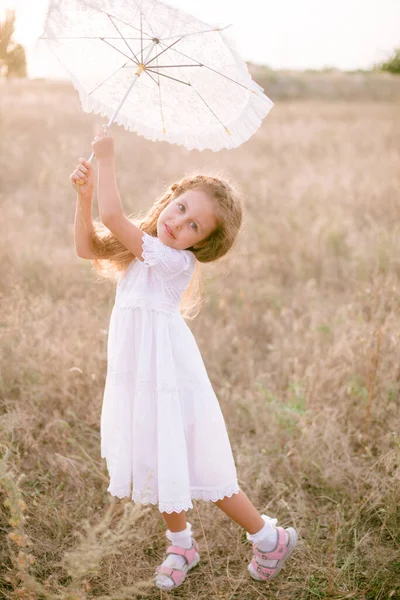 Yazın günbatımında kırsalda beyaz dantel şemsiyeli, uzun sarı kıvırcık saçlı, beyaz bir şapkası olan küçük şirin bir kız. Doğa ve Çevre Yaşamı