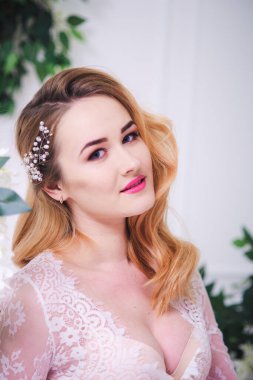 Sarı saçlı, düğün makyajlı, beyaz dantelli bir peignoir 'de parlak bir iç mekânda gelin buketi olan çekici bir gelin.