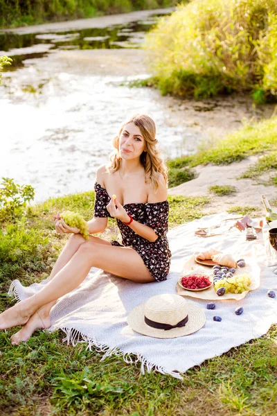 Young attractive girl with dark hair in a summer dress on a picnic in nature by the river in summer at sunset. Healthy life.