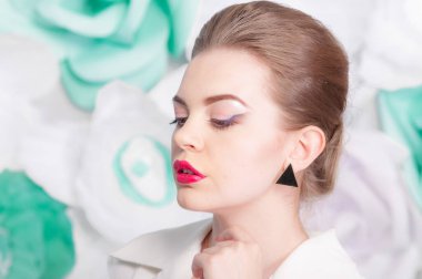 Young attractive girl with blond hair with trendy make-up and hairstyle in a white trendy jumpsuit with paper flowers decor