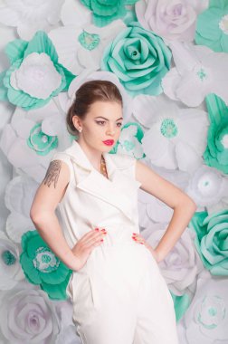 Young attractive girl with blond hair with trendy make-up and hairstyle in a white trendy jumpsuit with paper flowers decor