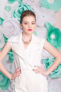 Young attractive girl with blond hair with trendy make-up and hairstyle in a white trendy jumpsuit with paper flowers decor