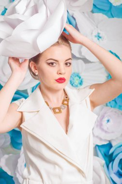 Young attractive girl with blond hair with trendy make-up and hairstyle in a white trendy jumpsuit with paper flowers decor