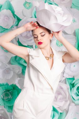 Young attractive girl with blond hair with trendy make-up and hairstyle in a white trendy jumpsuit with paper flowers decor