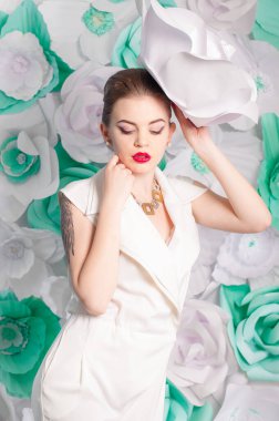 Young attractive girl with blond hair with trendy make-up and hairstyle in a white trendy jumpsuit with paper flowers decor