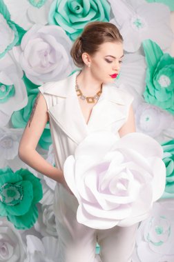 Young attractive girl with blond hair with trendy make-up and hairstyle in a white trendy jumpsuit with paper flowers decor