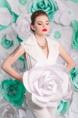 Young attractive girl with blond hair with trendy make-up and hairstyle in a white trendy jumpsuit with paper flowers decor
