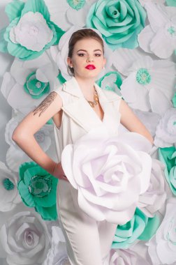 Young attractive girl with blond hair with trendy make-up and hairstyle in a white trendy jumpsuit with paper flowers decor