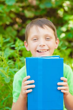 Cute boy in a green t-shirt with a school backpack and school books in the park. Back to school