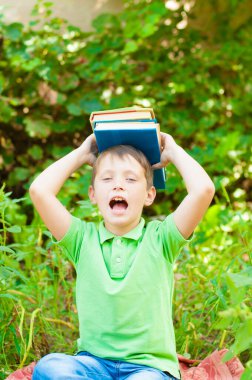 Cute boy in a green t-shirt with a school backpack and school books in the park. Back to school