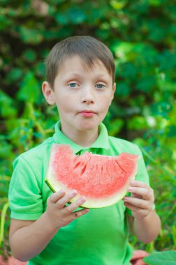 A cute boy in a green t-shirt eats a juicy ripe watermelon in the summer in the garden. Healthy lifestyle. Happy childhood