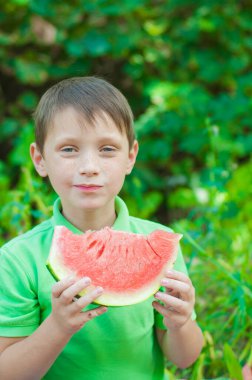 A cute boy in a green t-shirt eats a juicy ripe watermelon in the summer in the garden. Healthy lifestyle. Happy childhood