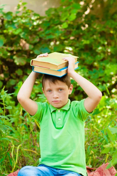 Cute boy in a green t-shirt with a school backpack and school books in the park. Back to school