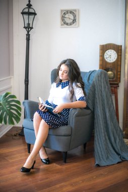 A cute teenage girl with long hair in a classic school dress in a classic interior with books and notebooks at the lesson. School life. Back to school