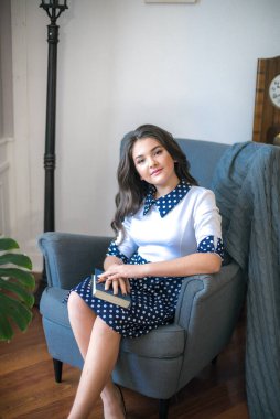 A cute teenage girl with long hair in a classic school dress in a classic interior with books and notebooks at the lesson. School life. Back to school