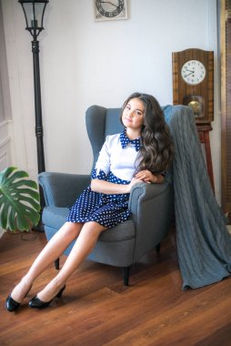 A cute teenage girl with long hair in a classic school dress in a classic interior with books and notebooks at the lesson. School life. Back to school