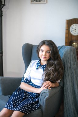 A cute teenage girl with long hair in a classic school dress in a classic interior with books and notebooks at the lesson. School life. Back to school