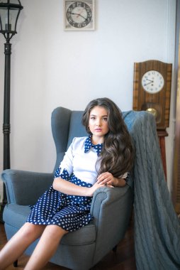 A cute teenage girl with long hair in a classic school dress in a classic interior with books and notebooks at the lesson. School life. Back to school