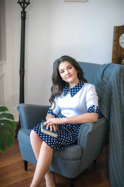 A cute teenage girl with long hair in a classic school dress in a classic interior with books and notebooks at the lesson. School life. Back to school