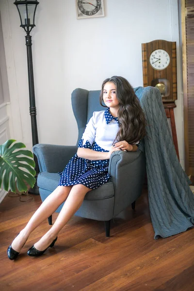 A cute teenage girl with long hair in a classic school dress in a classic interior with books and notebooks at the lesson. School life. Back to school