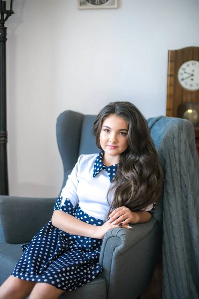 A cute teenage girl with long hair in a classic school dress in a classic interior with books and notebooks at the lesson. School life. Back to school
