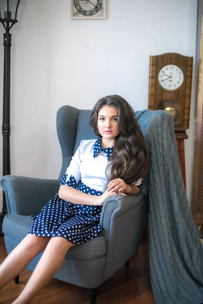 A cute teenage girl with long hair in a classic school dress in a classic interior with books and notebooks at the lesson. School life. Back to school