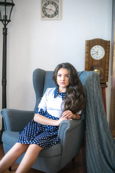 A cute teenage girl with long hair in a classic school dress in a classic interior with books and notebooks at the lesson. School life. Back to school