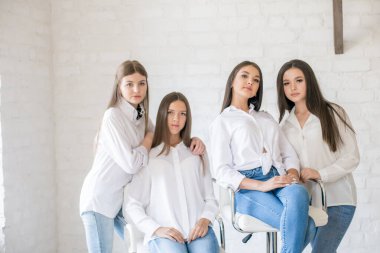 Pretty teenage girls models in trendy jeans and white shirts in the studio against the background of a white brick wall. Teenage fashion. beauty and fashion